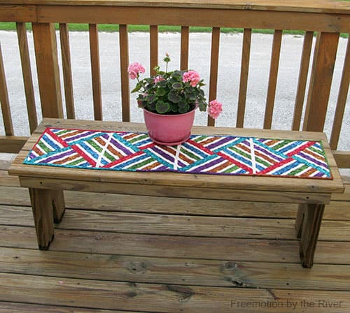 Bright Jewel strip pieced table runner on deck with flowers